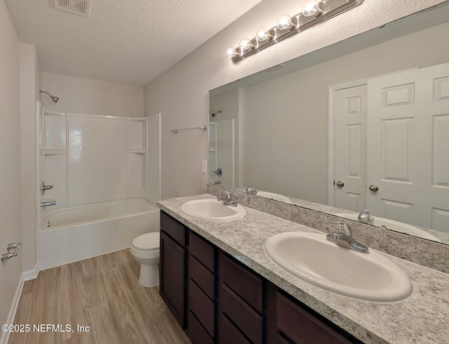 full bathroom with toilet, wood-type flooring, a textured ceiling, shower / tub combination, and vanity