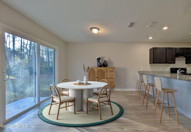 dining space featuring sink, light hardwood / wood-style flooring, and a textured ceiling