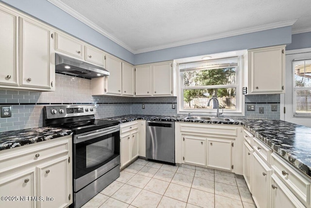 kitchen with stainless steel appliances, crown molding, cream cabinets, and dark stone countertops