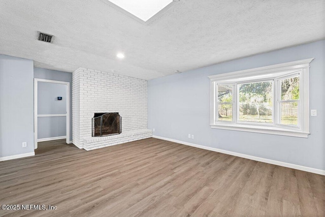 unfurnished living room featuring a textured ceiling, a brick fireplace, and light wood-type flooring