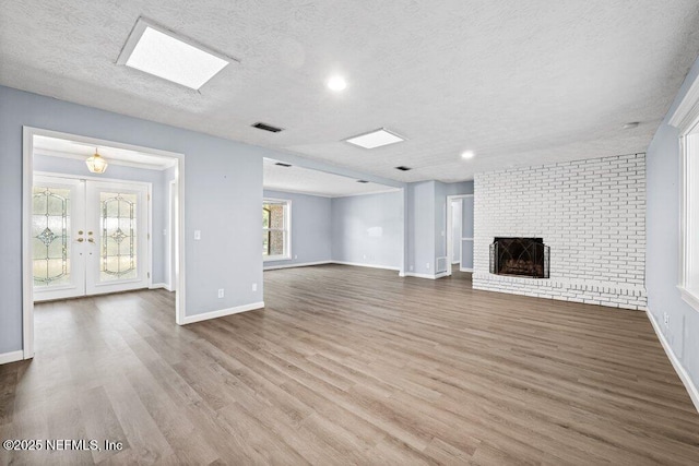 unfurnished living room with french doors, light hardwood / wood-style flooring, a brick fireplace, and a textured ceiling