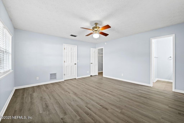 unfurnished bedroom featuring a spacious closet, a textured ceiling, dark hardwood / wood-style flooring, a closet, and ceiling fan