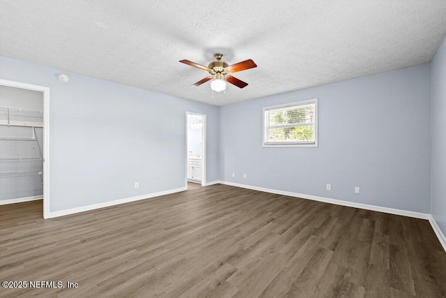 unfurnished bedroom featuring dark wood-type flooring, ceiling fan, a textured ceiling, a spacious closet, and a closet