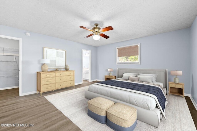 bedroom with ceiling fan, a walk in closet, dark wood-type flooring, and a textured ceiling