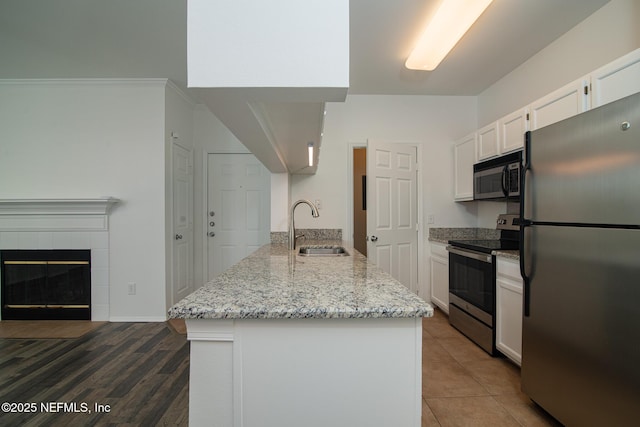 kitchen featuring appliances with stainless steel finishes, white cabinetry, sink, a tiled fireplace, and light stone counters