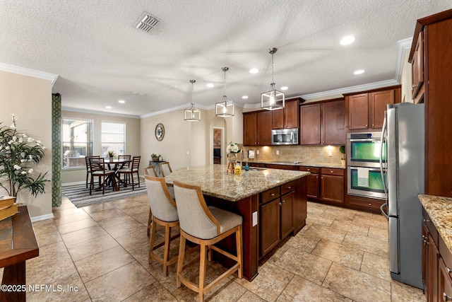 kitchen with a breakfast bar area, stainless steel appliances, light stone countertops, an island with sink, and decorative light fixtures