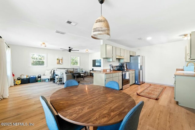 dining area with sink, ceiling fan with notable chandelier, and light hardwood / wood-style floors