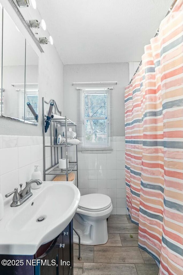 bathroom featuring walk in shower, vanity, toilet, and tile walls