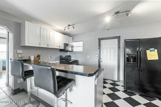 kitchen with black appliances, kitchen peninsula, white cabinets, and a breakfast bar