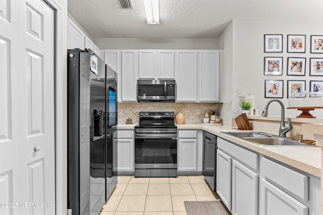 kitchen with sink, backsplash, light tile patterned floors, black appliances, and a textured ceiling