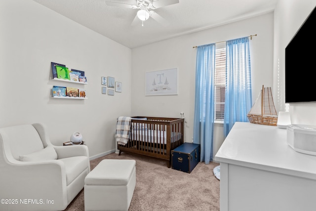 bedroom featuring a textured ceiling, light colored carpet, a nursery area, and ceiling fan