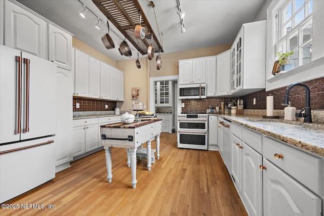 kitchen with white cabinetry, premium appliances, light stone countertops, and sink