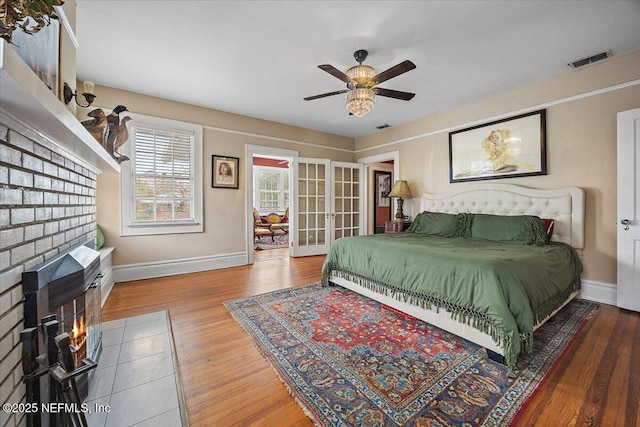 bedroom with french doors, ceiling fan, wood-type flooring, and a fireplace