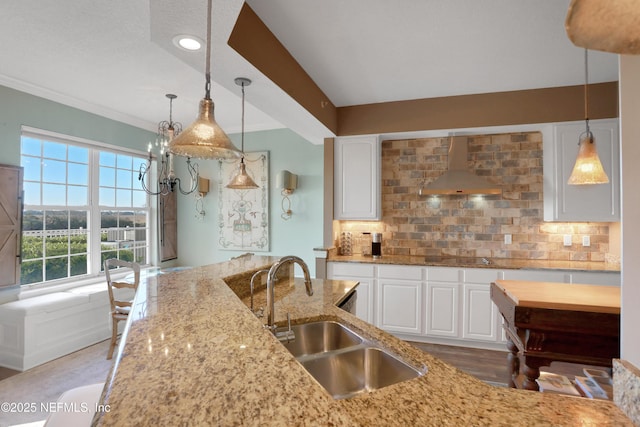 kitchen with wall chimney range hood, sink, white cabinetry, light stone countertops, and decorative backsplash