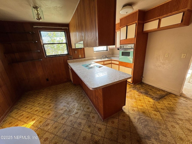 kitchen featuring wooden walls, stovetop, wall oven, kitchen peninsula, and a textured ceiling