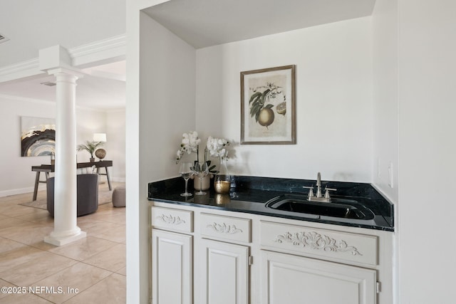 bar with sink, ornate columns, white cabinetry, crown molding, and light tile patterned floors