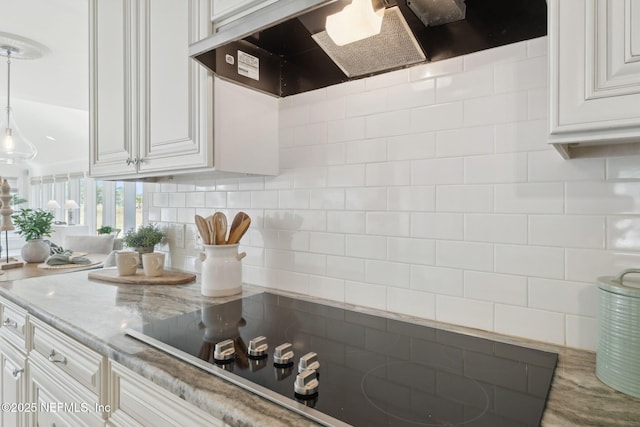 kitchen featuring light stone countertops, white cabinets, black electric cooktop, decorative light fixtures, and exhaust hood