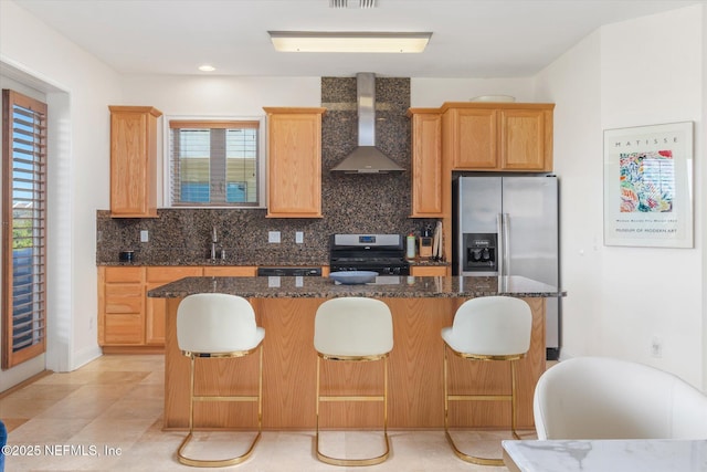 kitchen featuring stove, dark stone counters, wall chimney exhaust hood, and a kitchen island