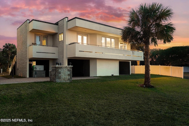 back house at dusk with a lawn and a balcony