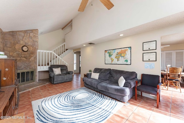 tiled living room with high vaulted ceiling, a stone fireplace, a textured ceiling, and ceiling fan