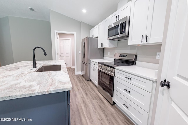 kitchen with appliances with stainless steel finishes, lofted ceiling, sink, white cabinets, and light stone countertops