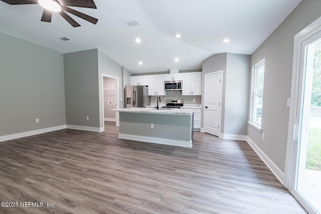 kitchen featuring white cabinetry, stainless steel appliances, wood-type flooring, an island with sink, and vaulted ceiling