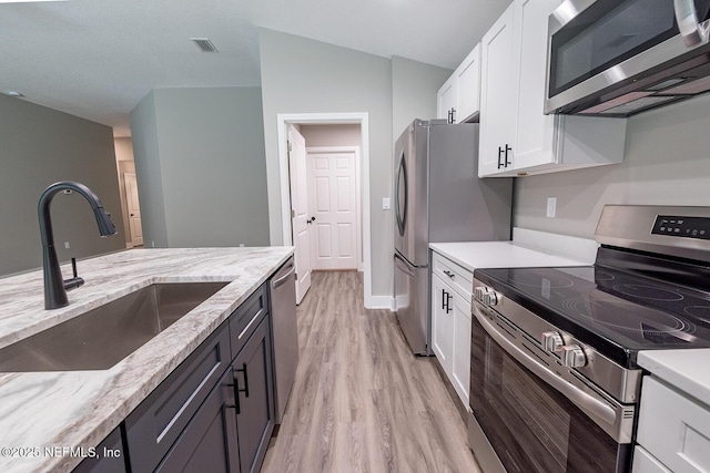 kitchen featuring sink, stainless steel appliances, light stone countertops, white cabinets, and light wood-type flooring