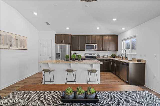 kitchen featuring a kitchen island, a breakfast bar, sink, stainless steel appliances, and light wood-type flooring