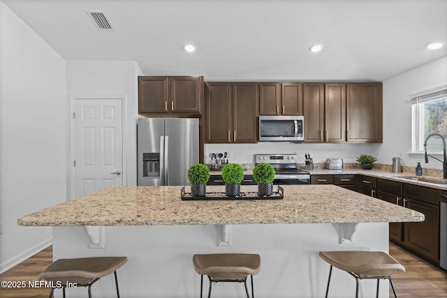 kitchen with sink, a center island, dark brown cabinets, hardwood / wood-style flooring, and stainless steel appliances