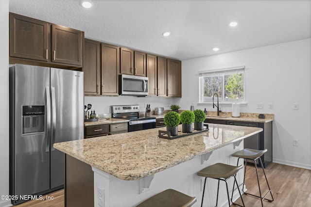 kitchen featuring sink, a breakfast bar area, appliances with stainless steel finishes, a center island, and dark brown cabinetry