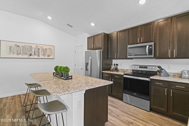 kitchen featuring vaulted ceiling, a kitchen island, a breakfast bar area, stainless steel appliances, and light wood-type flooring