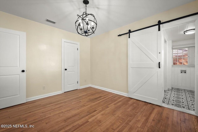 unfurnished room with an inviting chandelier, hardwood / wood-style flooring, and a barn door