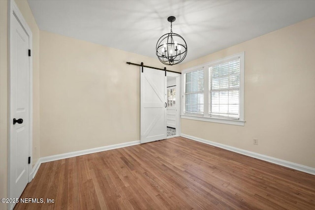 unfurnished dining area featuring a notable chandelier, wood-type flooring, and a barn door