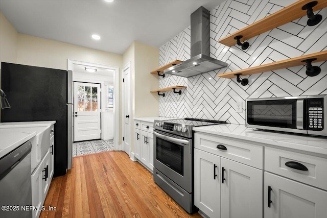 kitchen featuring white cabinetry, appliances with stainless steel finishes, island range hood, and light wood-type flooring