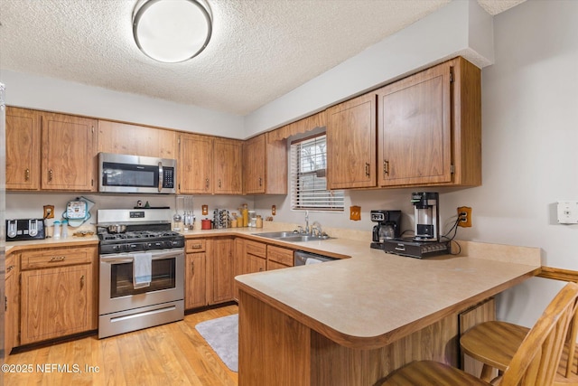 kitchen with sink, light hardwood / wood-style flooring, appliances with stainless steel finishes, a kitchen bar, and kitchen peninsula