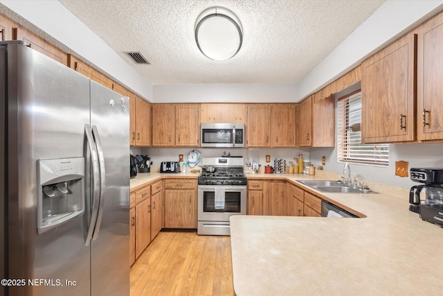 kitchen featuring appliances with stainless steel finishes, sink, light wood-type flooring, kitchen peninsula, and a textured ceiling