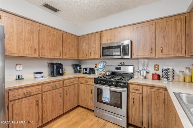 kitchen featuring stainless steel appliances, sink, light hardwood / wood-style flooring, and a textured ceiling