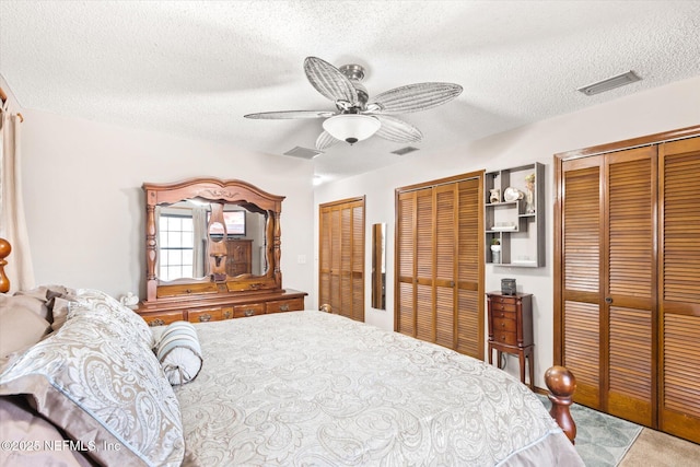 carpeted bedroom with ceiling fan, two closets, and a textured ceiling