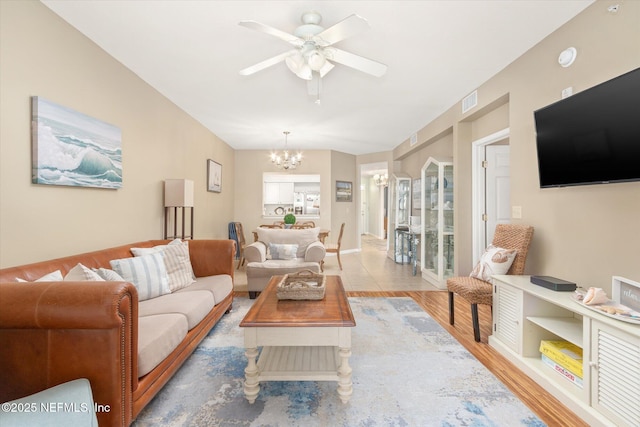 living room featuring ceiling fan with notable chandelier and light wood-type flooring