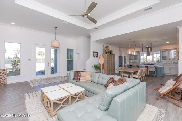 living room featuring light hardwood / wood-style flooring, ceiling fan, a tray ceiling, ornamental molding, and french doors