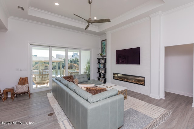 living room with crown molding, a raised ceiling, ceiling fan, and light wood-type flooring