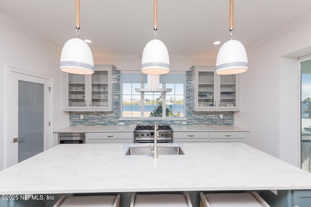 kitchen featuring gray cabinets, tasteful backsplash, stainless steel range, decorative light fixtures, and a large island with sink