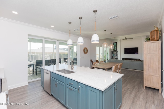 kitchen featuring blue cabinetry, sink, hanging light fixtures, stainless steel dishwasher, and an island with sink