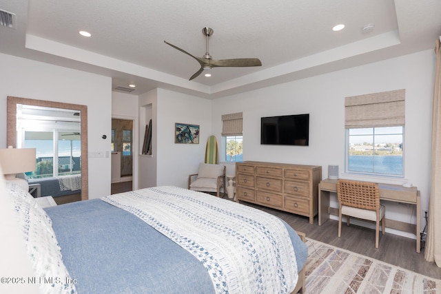 bedroom with multiple windows, hardwood / wood-style floors, and a raised ceiling