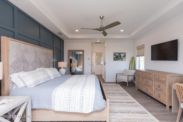 bedroom with ceiling fan, a tray ceiling, and light wood-type flooring