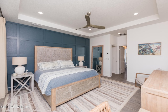 bedroom featuring hardwood / wood-style floors, a textured ceiling, and a tray ceiling