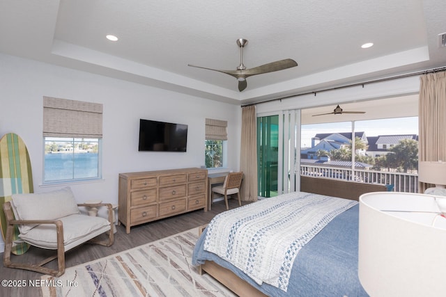 bedroom featuring wood-type flooring, a tray ceiling, access to exterior, and a textured ceiling