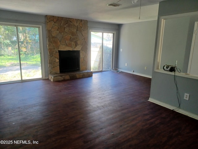 unfurnished living room with dark wood-type flooring and a stone fireplace