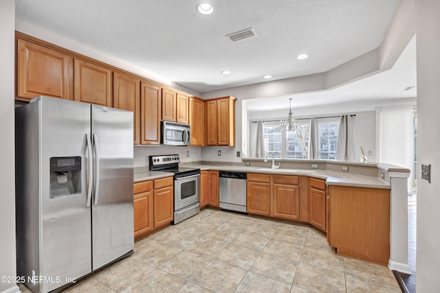 kitchen featuring light tile patterned flooring, appliances with stainless steel finishes, pendant lighting, kitchen peninsula, and a textured ceiling