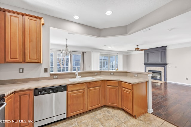 kitchen featuring ceiling fan with notable chandelier, dishwasher, sink, a large fireplace, and kitchen peninsula